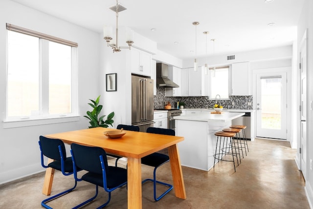 kitchen with pendant lighting, high quality appliances, wall chimney exhaust hood, a kitchen island, and white cabinetry