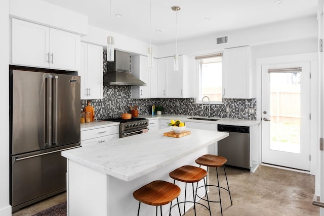 kitchen with high end appliances, sink, wall chimney exhaust hood, a kitchen island, and white cabinetry