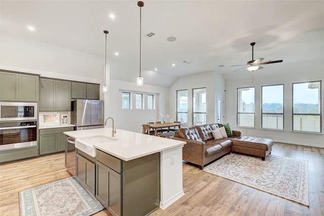 kitchen featuring lofted ceiling, a center island with sink, light wood-type flooring, appliances with stainless steel finishes, and pendant lighting