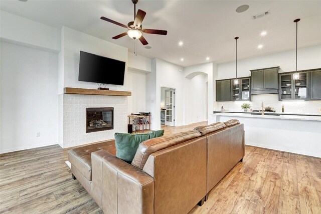 living room featuring a tiled fireplace, ceiling fan, sink, and light wood-type flooring