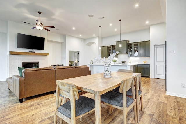 dining area with a brick fireplace, light hardwood / wood-style flooring, and ceiling fan