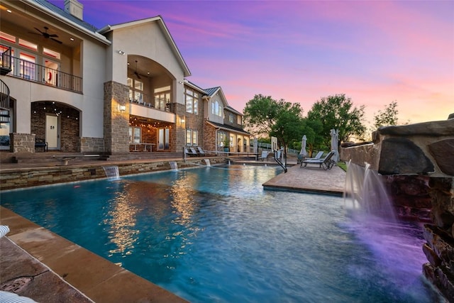 pool at dusk with pool water feature, ceiling fan, and a patio area