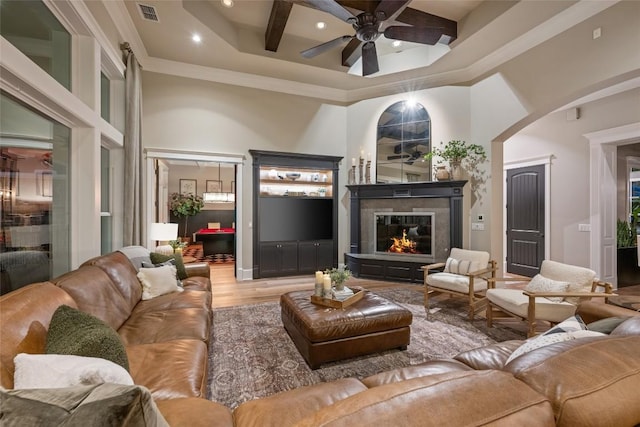 living room with hardwood / wood-style flooring, ceiling fan, a towering ceiling, ornamental molding, and beam ceiling