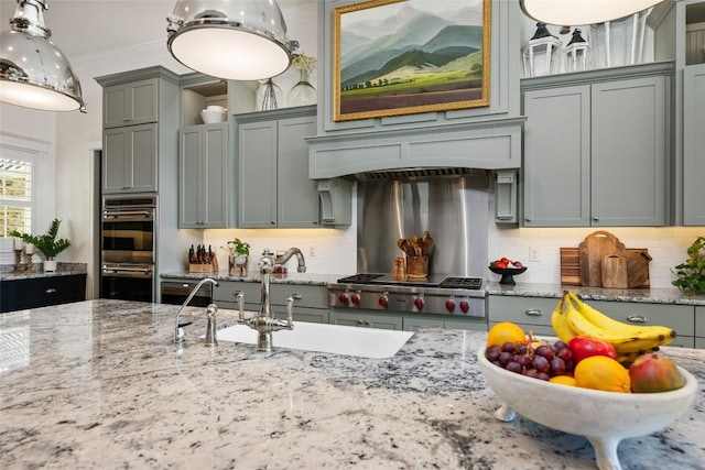 kitchen featuring tasteful backsplash, light stone counters, pendant lighting, and custom range hood