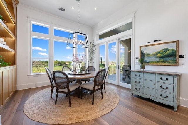 dining space with an inviting chandelier, crown molding, dark wood-type flooring, and french doors