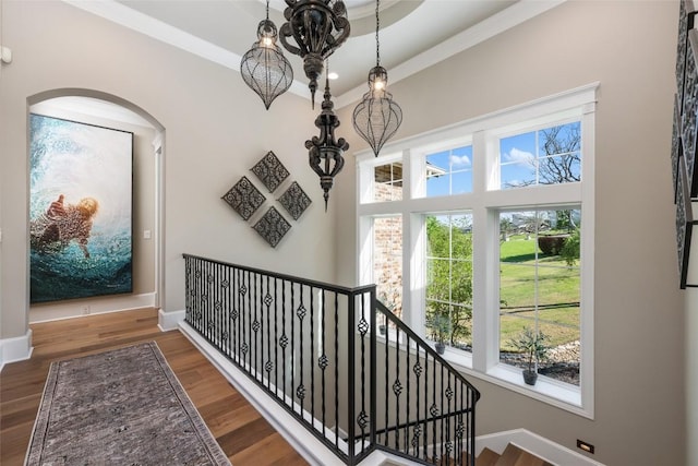 stairs with ornamental molding, wood-type flooring, and an inviting chandelier