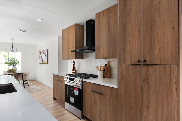 kitchen with tasteful backsplash, stainless steel gas range oven, wall chimney exhaust hood, pendant lighting, and a notable chandelier