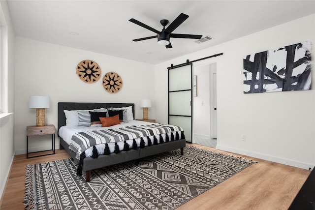 bedroom featuring wood-type flooring, a barn door, and ceiling fan