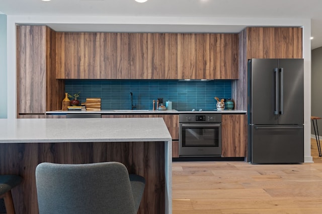 kitchen featuring a kitchen bar, appliances with stainless steel finishes, tasteful backsplash, sink, and light hardwood / wood-style floors