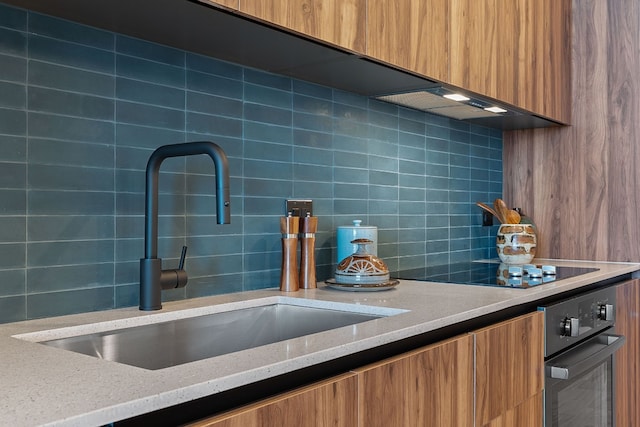 kitchen with backsplash, oven, light stone countertops, and sink