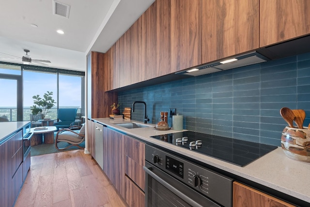 kitchen featuring black electric stovetop, stainless steel oven, ceiling fan, sink, and light hardwood / wood-style flooring