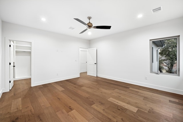 unfurnished bedroom featuring ceiling fan, a walk in closet, a closet, and dark hardwood / wood-style floors