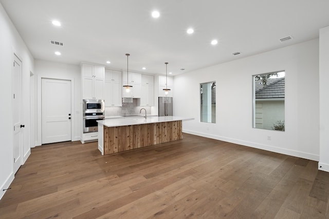 kitchen featuring white cabinetry, a large island, appliances with stainless steel finishes, tasteful backsplash, and hanging light fixtures