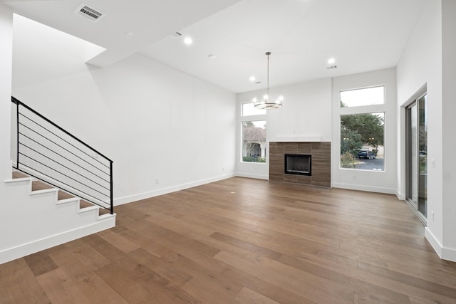 unfurnished living room with a high ceiling, an inviting chandelier, wood-type flooring, and a tiled fireplace