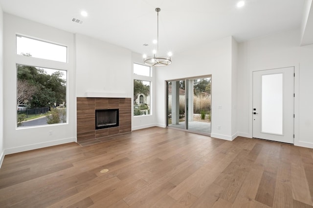 unfurnished living room featuring light wood-type flooring, a notable chandelier, a towering ceiling, and a tiled fireplace