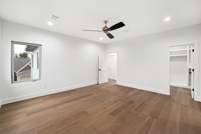 unfurnished bedroom with ceiling fan, a walk in closet, a closet, and dark hardwood / wood-style floors