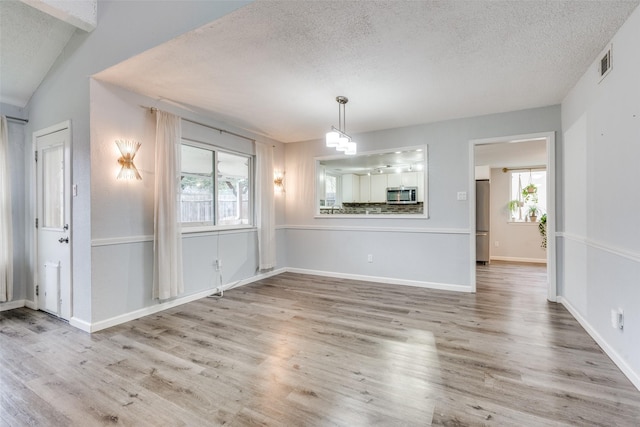 unfurnished dining area with hardwood / wood-style floors, a textured ceiling, and vaulted ceiling