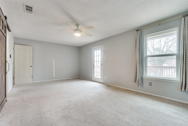 carpeted empty room featuring ceiling fan and a barn door