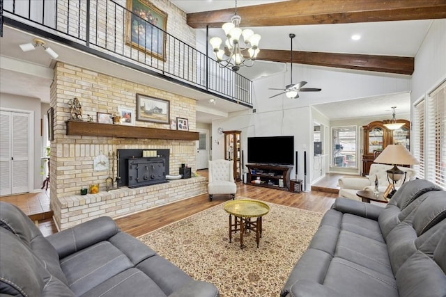 living room featuring beam ceiling, a wood stove, ceiling fan with notable chandelier, and light wood-type flooring