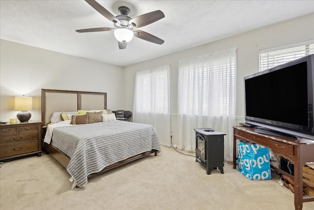 bedroom featuring light carpet, a wood stove, and ceiling fan