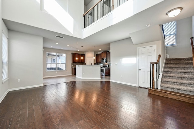 unfurnished living room with baseboards, visible vents, dark wood finished floors, stairway, and a high ceiling