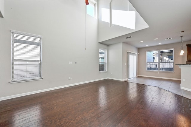 unfurnished living room featuring plenty of natural light, baseboards, visible vents, and wood finished floors