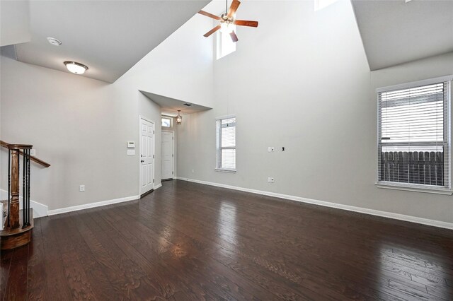 unfurnished living room with a towering ceiling, a ceiling fan, stairs, baseboards, and dark wood finished floors