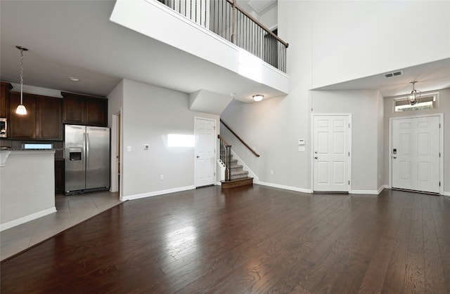 unfurnished living room featuring visible vents, a high ceiling, wood finished floors, baseboards, and stairs