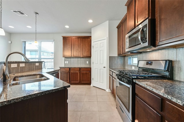 kitchen featuring pendant lighting, light tile patterned floors, appliances with stainless steel finishes, a sink, and dark stone counters