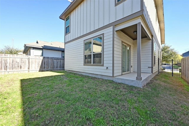 rear view of house with a patio, board and batten siding, a fenced backyard, and a lawn