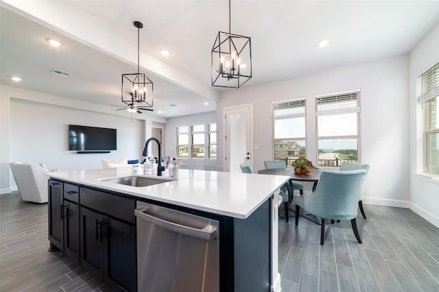 kitchen featuring stainless steel dishwasher, ceiling fan, a kitchen island with sink, sink, and hanging light fixtures