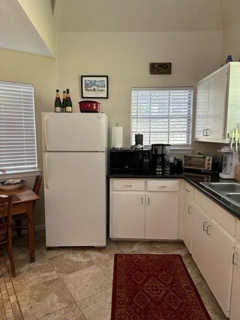 kitchen with light tile patterned floors, white fridge, white cabinetry, and sink