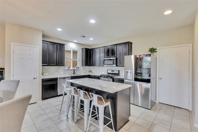 kitchen with a center island, sink, appliances with stainless steel finishes, tasteful backsplash, and light stone counters