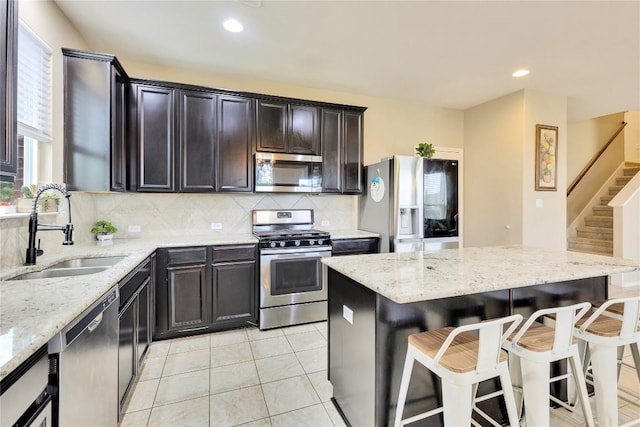 kitchen with sink, decorative backsplash, light stone countertops, appliances with stainless steel finishes, and light tile patterned flooring