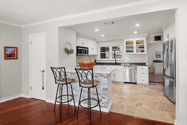 408 Silver Spur, Horseshoe Bay, TX 78657 - kitchen with appliances with stainless steel finishes, a kitchen bar, decorative backsplash, white cabinets, and crown molding