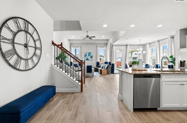 kitchen with light stone counters, ceiling fan with notable chandelier, sink, dishwasher, and white cabinetry