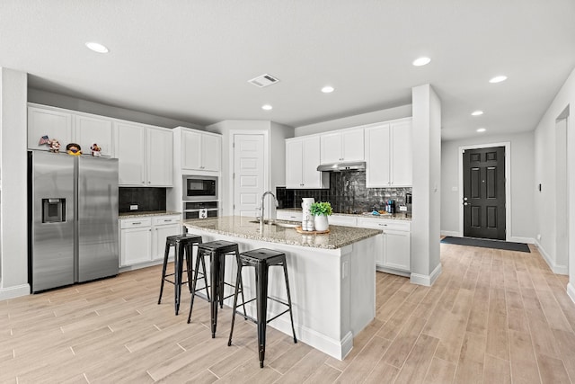 kitchen with a kitchen bar, light stone countertops, stainless steel appliances, a kitchen island with sink, and white cabinetry