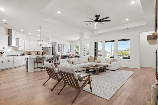 living area with recessed lighting, a raised ceiling, and light wood-style flooring