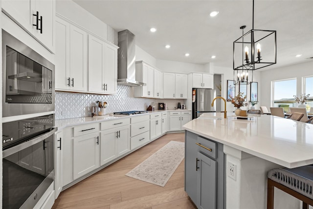 kitchen with white cabinets, light countertops, a center island with sink, and wall chimney range hood