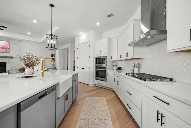 kitchen featuring decorative light fixtures, sink, white cabinetry, wall chimney range hood, and stainless steel appliances