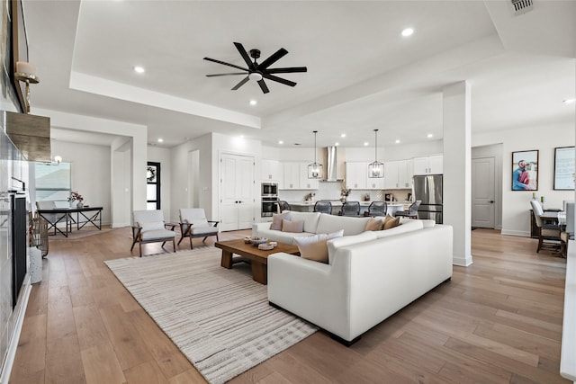 living room with ceiling fan, a tray ceiling, and light hardwood / wood-style flooring