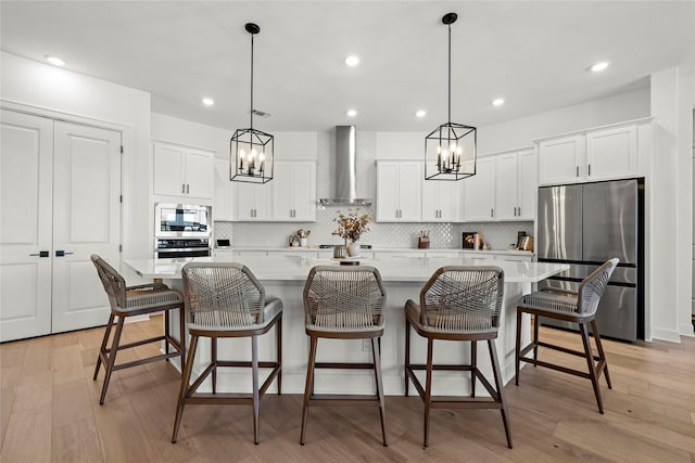 kitchen featuring appliances with stainless steel finishes, light countertops, wall chimney range hood, and a spacious island