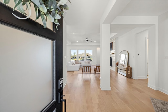 foyer entrance featuring light wood finished floors, baseboards, a ceiling fan, a fireplace, and recessed lighting