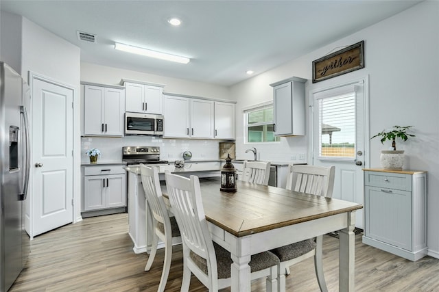 kitchen featuring appliances with stainless steel finishes, light hardwood / wood-style floors, gray cabinets, and tasteful backsplash