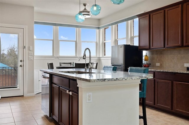 kitchen featuring pendant lighting, a kitchen island with sink, sink, light stone countertops, and appliances with stainless steel finishes