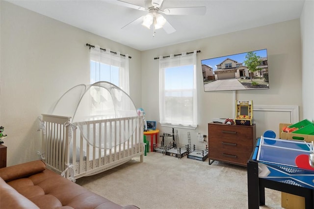 carpeted bedroom featuring ceiling fan and a nursery area