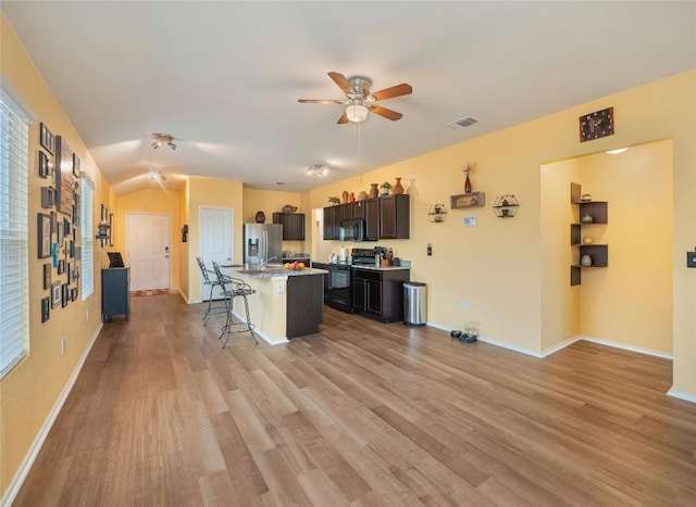 kitchen with ceiling fan, light hardwood / wood-style flooring, a kitchen bar, a kitchen island with sink, and black appliances