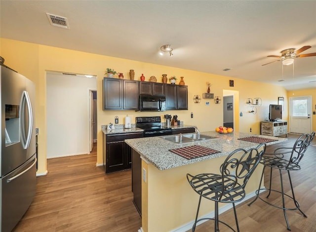 kitchen featuring a breakfast bar, black appliances, hardwood / wood-style flooring, an island with sink, and dark brown cabinets