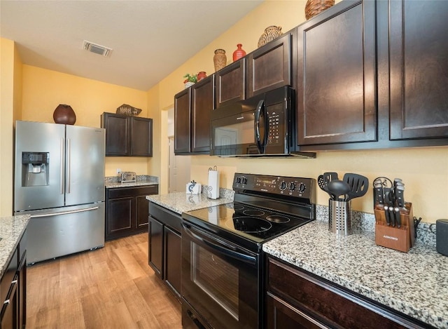 kitchen featuring light stone counters, dark brown cabinets, black appliances, and light hardwood / wood-style flooring