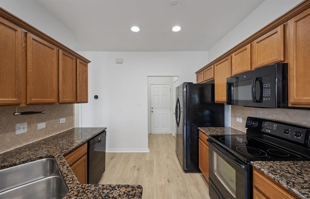 kitchen featuring tasteful backsplash, light hardwood / wood-style flooring, dark stone counters, and black appliances